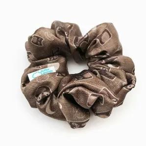 Satin scrunchie featuring a scruffy but sweet werewolf on a brown background with moons.<br>The silky satin fabric makes for a snag-free hair experience. Wrap around a ponytail or bun for a fun pop of Halloween season spirit.<br>Inner elastic stretches from approximately 2" to 7" wide. The whole scrunchie measures approximately 5" in diameter when unstretched.